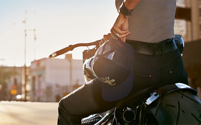 In the close-up, a motorcyclist has the Boxer cap from the collection in her hand and is wearing the RoadCrafted jeans for women.