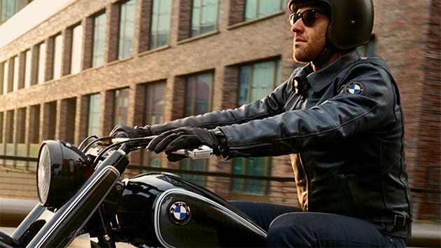 A driver sits relaxed on his motorcycle, wearing a Pureboxer men’s leather jacket.